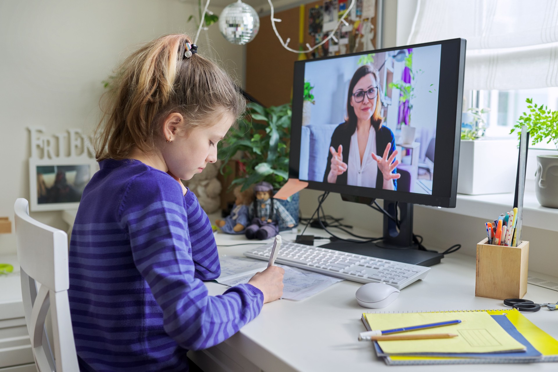 Child girl studying with teacher remotely on computer using video call